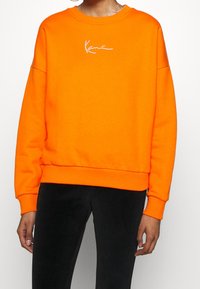Felpa arancione con scollo rotondo e vestibilità rilassata, caratterizzata da un ricamo bianco del logo sul petto e polsini e orlo a costine.