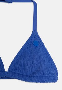 Blå strikket trekant bikini-top med justerbare stropper, teksturert mønster og en sirkulær blå logo-akse på høyre side.