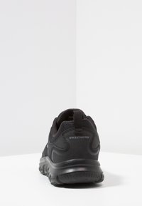 Black athletic shoe featuring a textured mesh upper, padded collar, pull tab, and thick rubber sole with a flexible design.