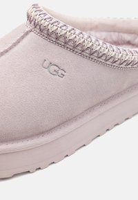 Lila mockasins i mocka med flätad kant, UGG-logotyp och en texturerad sula. Den mjuka ovandelen har en rundad form för en snug passform.