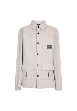 Helle beige Jacke mit langen Ärmeln, Knopfriegel, spitzem Kragen, zwei Vordertaschen und einer Brusttasche mit einem Logopatch.