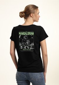 Svart bomull t-shirt med en färgglad grafisk tryck på ryggen som föreställer karaktärer och text från "The Mandalorian." Korta ärmar.