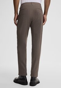 Brązowe spodnie z elastycznym pasem, slim fit, subtelny wzór w kratkę, dwie tylne kieszenie, zestawione z czarnymi botkami za kostkę.