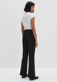 Pantaloni neri a palazzo con una texture liscia, vita alta e tasche posteriori, abbinati a una maglietta bianca aderente a maniche corte.