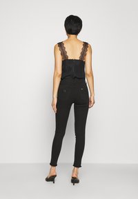 Camisón de encaje negro con tirantes, con rayas verticales, combinado con jeans ajustados negros de talle alto con dobladillo desgastado. Zapatos planos.