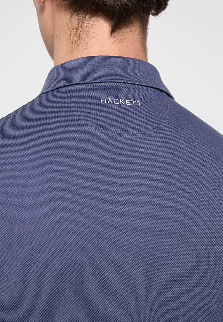 T-shirt polo bleu marine en tissu texturé, avec un col replié et le logo blanc "HACKETT" au dos, mettant en avant des détails de design modernes.