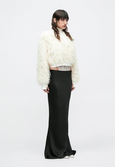 Λευκό, αφράτο cropped πουλόβερ με μακριά μανίκια, συνδυασμένο με μαύρη σατέν φούστα μέχρι το πάτωμα. Διακρίνεται καθαρά εσώρουχο στη μέση.