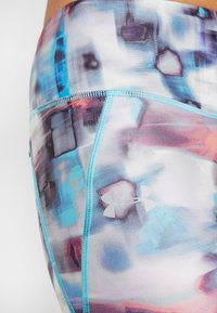 Väriküllased atleetikatte lühikesed püksid, millel on erksavärviline abstraktne muster sinise, lilla ja roosa tooni ning kontrastsete helesiniste õmblustega, samuti Under Armouri logo.