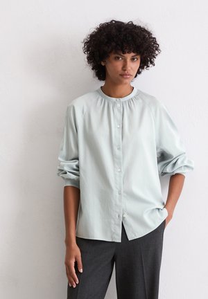 Lichtblauw button-up overhemd met een ronde halslijn en geplooide details bij de schouders. Voorzien van lange mouwen met manchetten en een relaxte pasvorm.