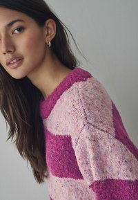 Strickpullover mit pink und lila gestreiften Mustern und einer strukturierten Oberfläche. Runder Halsausschnitt und gerippte Bündchen. Weiche Wollmischung.