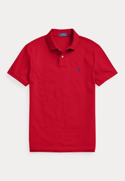 Κόκκινο πόλο με κοντά μανίκια, δύο λευκά κουμπιά και μικρό μπλε κεντητό λογότυπο στο αριστερό μέρος του στήθους.