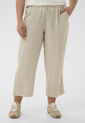 Beige en wit verticale gestreepte cropped broek met een trekkoord in de taille, gedragen met beige sneakers op een neutrale achtergrond.