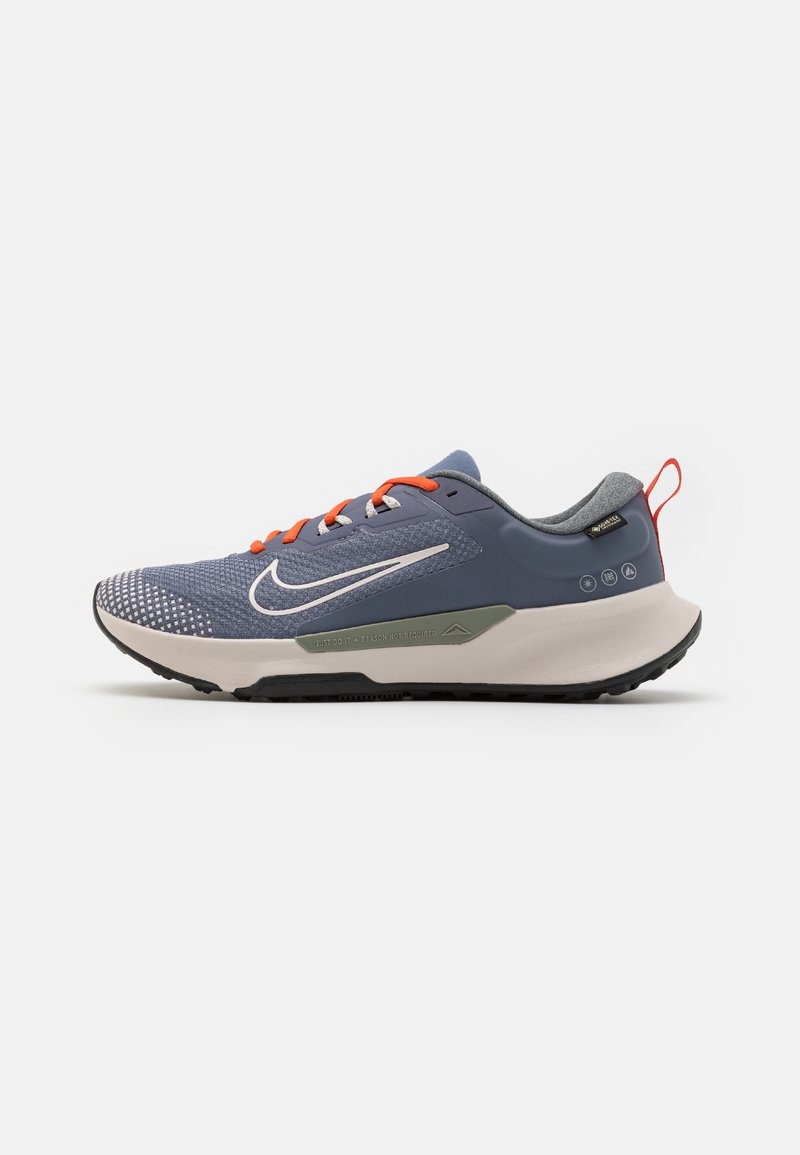 Chaussure de course bleue et grise avec semelle blanche, lacets orange, logo Nike blanc et boucle rouge au talon, montrée de profil sur fond blanc.