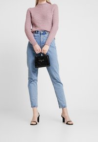 Light pink, textured knit sweater paired with high-waisted, light blue jeans. Black, patent leather mini handbag and black heeled sandals.