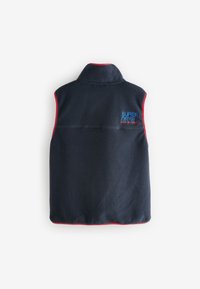 Tamsiai mėlynas fliso liemenė su aukštu apykakliu, raudonu apvadu ir siuvinėtu "SUPERDRY" logotipu mėlyna spalva kairėje pusėje. Minkšta tekstūra ir be rankovių dizainas.