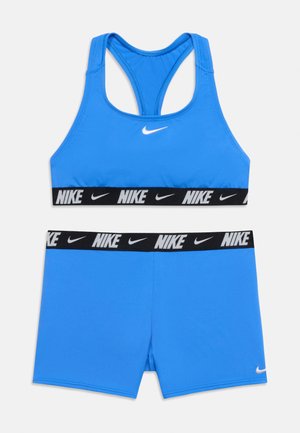 Ensemble brassière de sport Nike bleue et short assorti avec bandes élastiques noires ornées de logos Nike blancs et de swooshes.