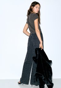 Siv bombažna majica, široke črne hlače z teksturo in črna šala iz umetnega krzna. Model stoji z obrnjenimi hrbtom, obut v sandale s paščki.