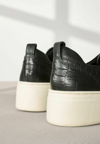 Schwarze Ledersneaker mit einem strukturierten Krokodilmuster und weißen Plateausohlen. Verfügt über abgerundete Kanten und Akzentnähte.