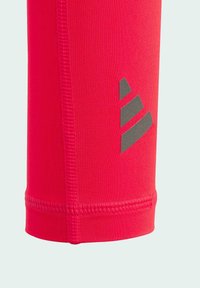 Rote sportliche Leggings mit eng anliegendem Schnitt, ausgestattet mit einem strukturierten Taillenbund und einem dunkelgrauen Logodesign an der Seite. Glattes, dehnbares Material.