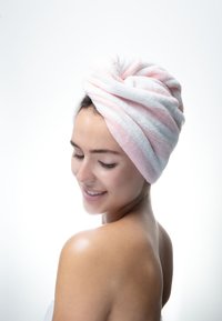 Serviette rayée blanche et rose enroulée autour de la tête d'une femme, mettant en valeur une texture douce et un design torsadé. Épaule nue et lisse visible.