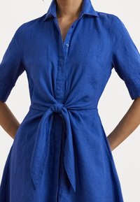 Blå linneskjortklänning med krage, korta ärmar och knytmidja. Har en knapplist framtill och en mjuk textur.