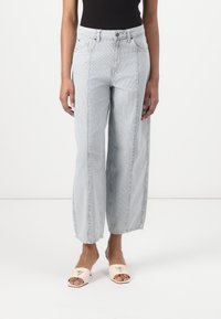 Lyseblå, vide jeans med vertikale striper, fem lommer og knappestolpe. Stoffet har en glatt tekstur. Kombinert med nude sandaler.
