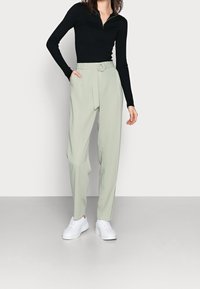 Haut noir côtelé à manches longues avec col zippé, associé à un pantalon taille haute vert clair, ceinturé et à coupe décontractée ; baskets blanches.