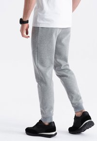 Grijze sweatpants met taps toelopende pijpen, elastische boorden en zijzakken, gecombineerd met zwarte sportschoenen op een effen achtergrond.