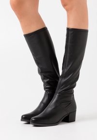 Bottes en cuir noir montant jusqu'aux genoux avec un design élégant, dotées d'un bout carré et d'un talon épais. Texture lisse avec des détails de couture subtils.