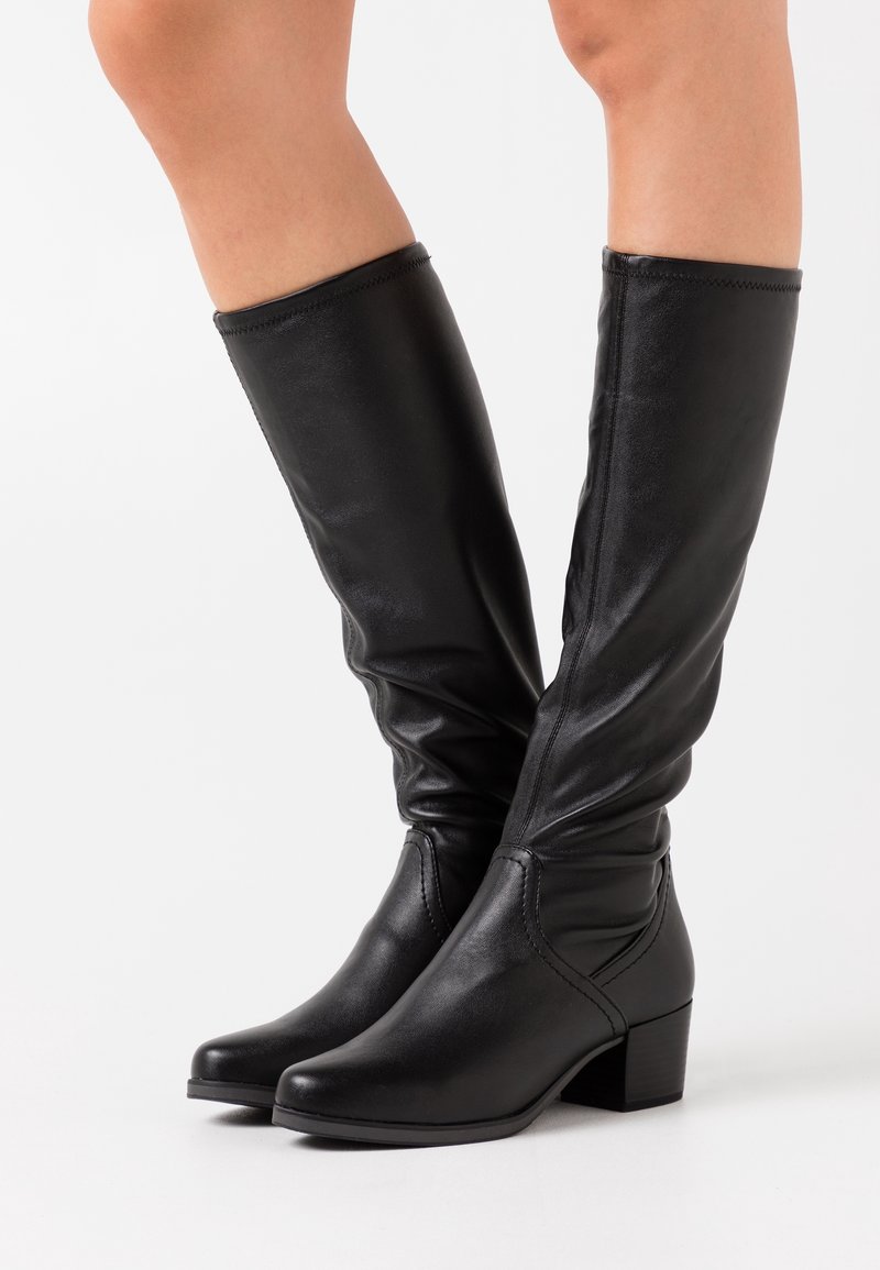 Bottes en cuir noir montant jusqu'aux genoux avec un design élégant, dotées d'un bout carré et d'un talon épais. Texture lisse avec des détails de couture subtils.