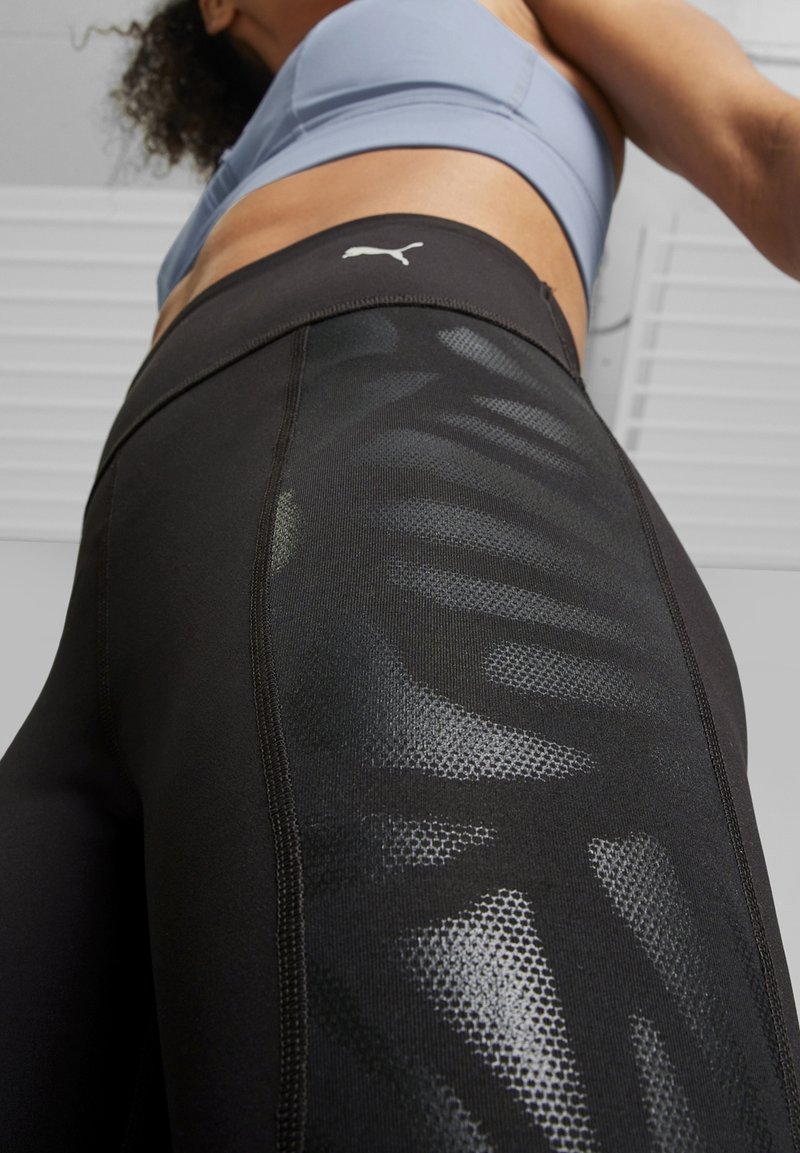 Leggings atletici neri con un motivo a rete, caratterizzati da una texture liscia e un design aderente. Presentano un piccolo logo bianco sulla fascia in vita.