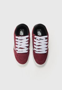 Red suede sneakers with white laces and a black interior. Features a white side stripe and a textured rubber sole.