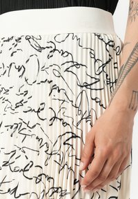 Jupe plissée avec un motif de lignes abstraites noires sur un fond crème, dotée d'une large ceinture blanche et d'un tissu doux et texturé.