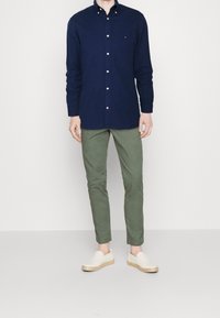 Námořnická dlouhá košile s knoflíky, olivové chinos kalhoty a béžové slip-on boty s tkanou jutu podešví. Jednoduchý design, bez viditelných vzorů.