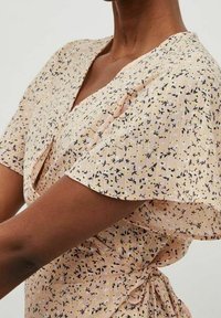 Vaaleanpunaisesta kankaasta valmistettu kukkakuvioinen kietaisumekko, jossa on lyhyet hihat ja mustia sekä keltaisia kuvioita. Sivulla oleva solmimisnauha antaa rakenteen.