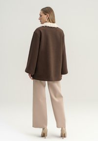 Maglione oversize marrone con un colletto testurizzato color crema, abbinato a pantaloni beige a gamba larga e scarpe con tacco nudo.