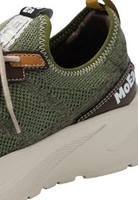 Grønne strikkede sneakers med en teksturert stoffoverdel, beige mellomsåle og brune skinnakcenter med kontrastfarget hvit søm.