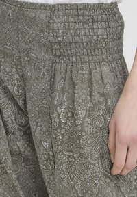 Gros plan sur un pantalon en tissu vert à motifs avec une taille élastique froncée et une main posée à côté.