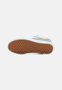 Grønn semsket sneakersåle med hvit gummibelegg og teksturert brun gummisåle med diamantmønster for trekkraft og grep.