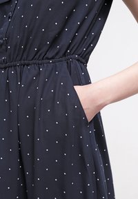 Marinblå klänning med vita prickar, med elastisk midja och sidofickor, gjord av ett mjukt tyg, som visar upp en avslappnad passform.