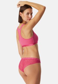 Růžový sportovní podprsenka a sada krajkového spodního prádla. Podprsenka se vyznačuje hladkým materiálem a širokým páskem, zatímco spodní prádlo má květinový krajkový design a elastický pas.