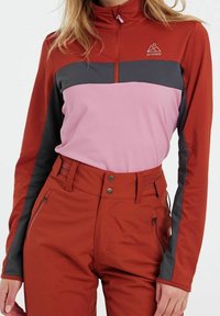 Langärmliges, zip-up Oberteil in Rot-, Rosa- und Graufarbenblock. Verfügt über einen hohen Kragen und atmungsaktiven Stoff. Getragen mit passenden, hoch geschnittenen Hosen.