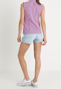 Top sin mangas de rayas moradas y blancas con hombros volantes, combinado con pantalones cortos de mezclilla claros y zapatillas blancas. Look simple y casual.