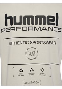 Beige t-shirt med stor svart text som står "hummel PERFORMANCE" och "AUTHENTIC SPORTSWEAR." Innehåller olika ikoner och en cirkulär design.