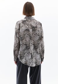 Halenka s dlouhým rukávem v leopardím vzoru, s límečkem, detailem na zadním díle a zakřiveným lemem z lehkého materiálu.