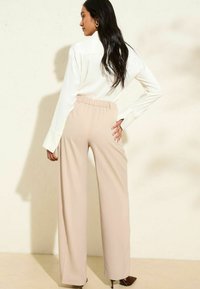Pantalons beige à jambes larges avec une taille élastique, associés à une chemise blanche à manches longues. Tissu lisse avec un minimum d'élasticité.