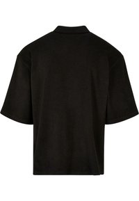 Polo negro de manga corta con una textura suave, cuello tradicional y un corte relajado. La parte posterior es sencilla y sin adornos.