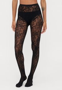 Collants en dentelle noire avec un motif floral, taille haute et texture lisse, offrant un aspect transparent avec des accents doux et opaques.