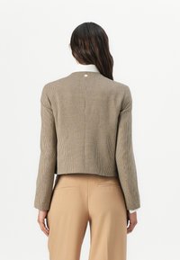 Blazer marrone a scacchi con un design cropped, dotato di maniche lunghe e colletto bianco a contrasto. Dettaglio hardware sottile sul retro.
