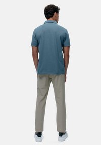 Férfi rövidujjú pólóing antracitkék színben, puha anyagból készült, lapos gallérral és hátvarrással, világos bézs nadrággal párosítva.